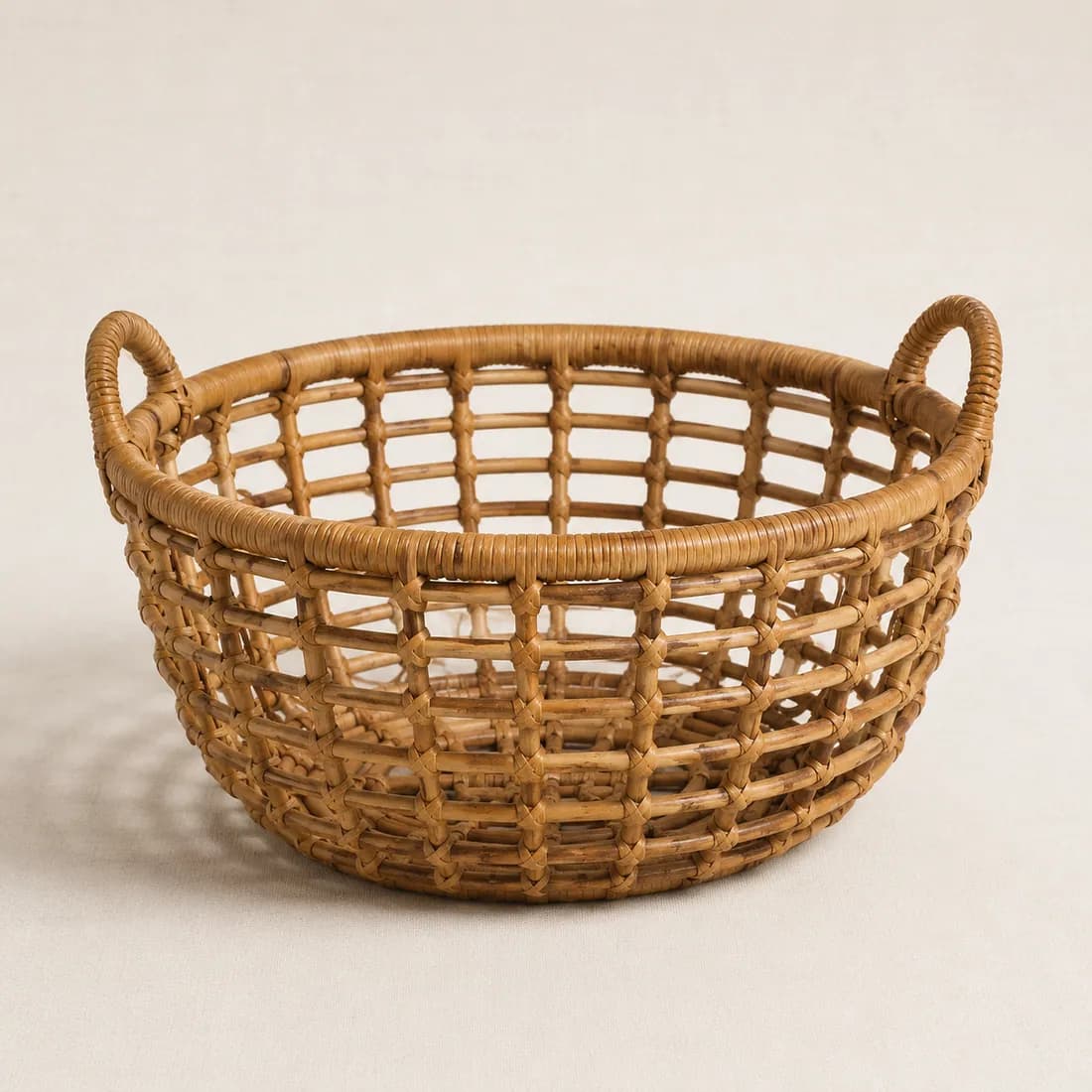 A sturdy round rattan basket with heavy open lattice weave and two woven side handles, shown empty.