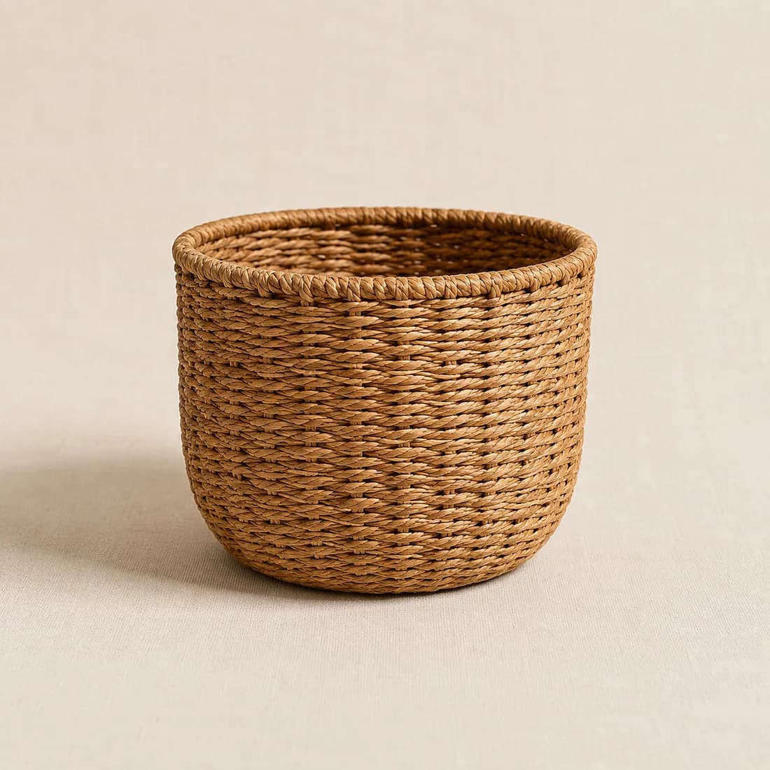 A round woven pot cover in warm honey-beige fibre with a rolled rim, shown empty.