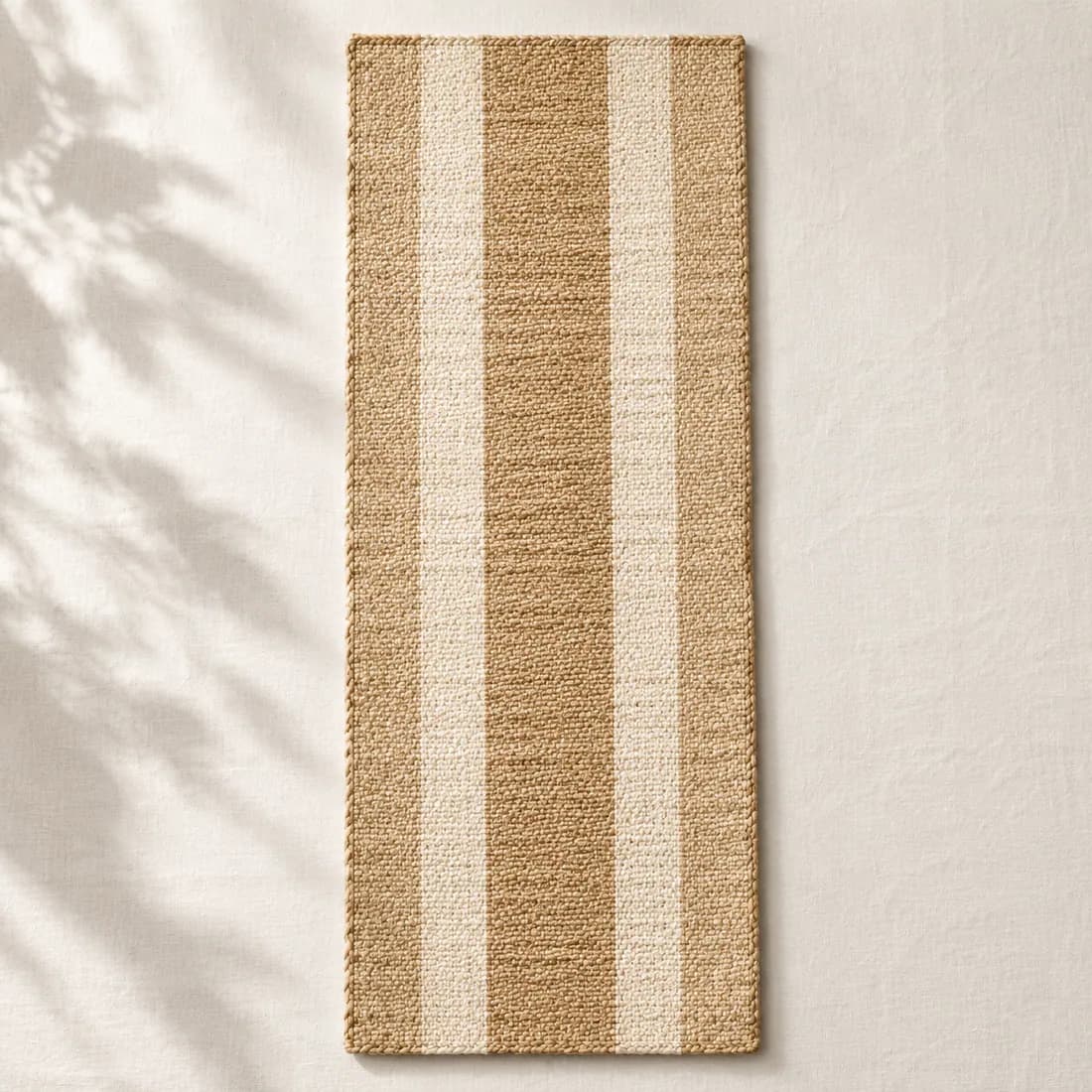 A long woven table runner in pale straw and beige bands, laid flat and empty.