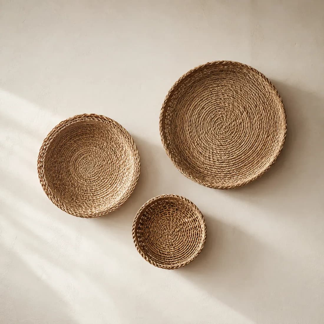 Three flat-backed round wall baskets of different sizes arranged on a pale plaster wall.